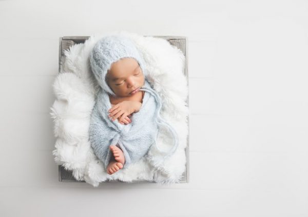 newborn baby on white fluff, in gray blanket