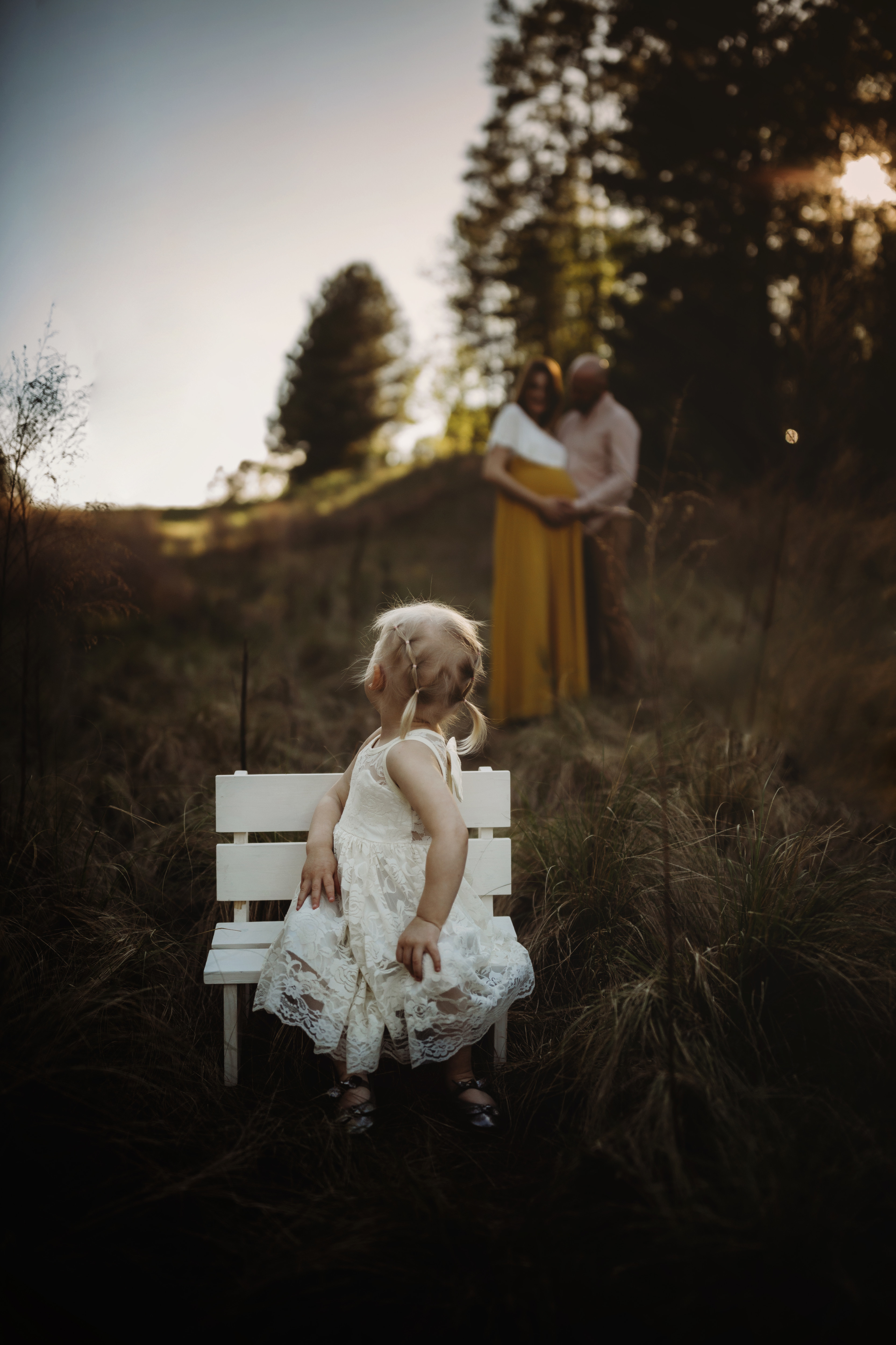 little girl on bench in foreground, parents in background, twins maternity photography