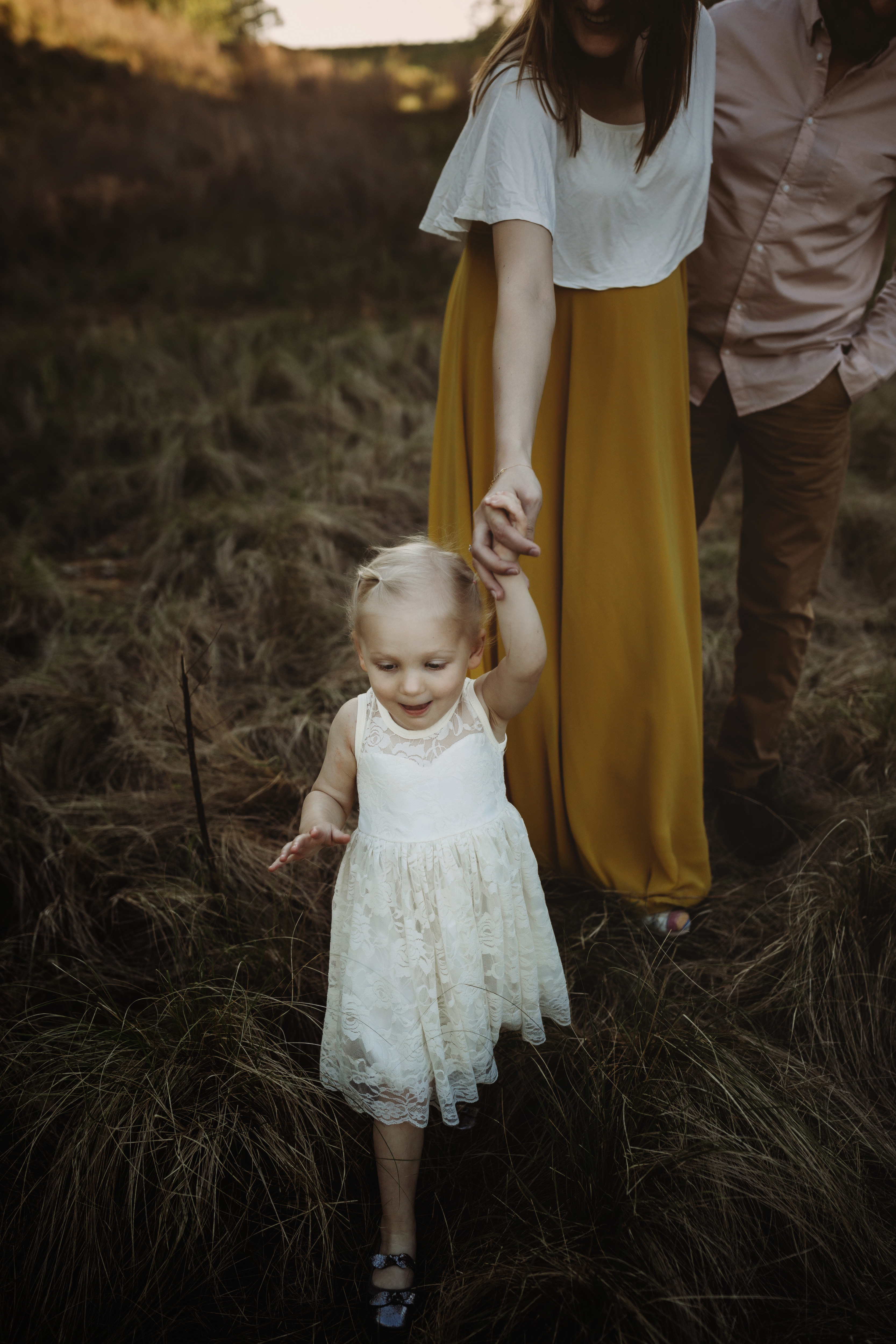 little girl in white dress in foreground, holding mother's hand, twins maternity photography